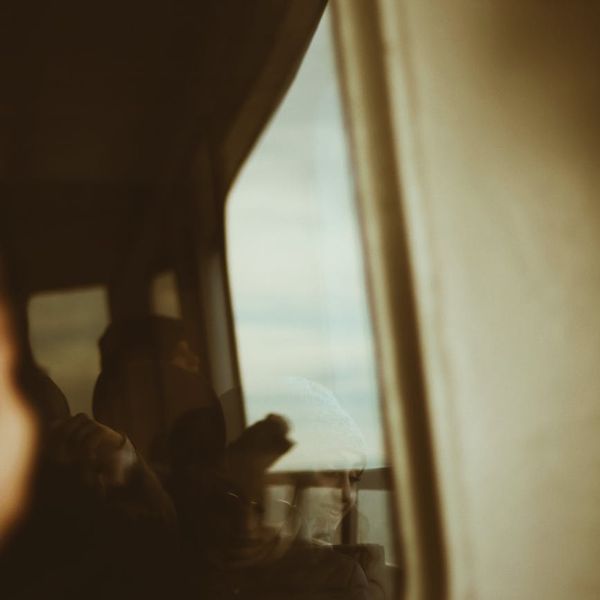 Person looking thoughtfully at a serene landscape through a window.